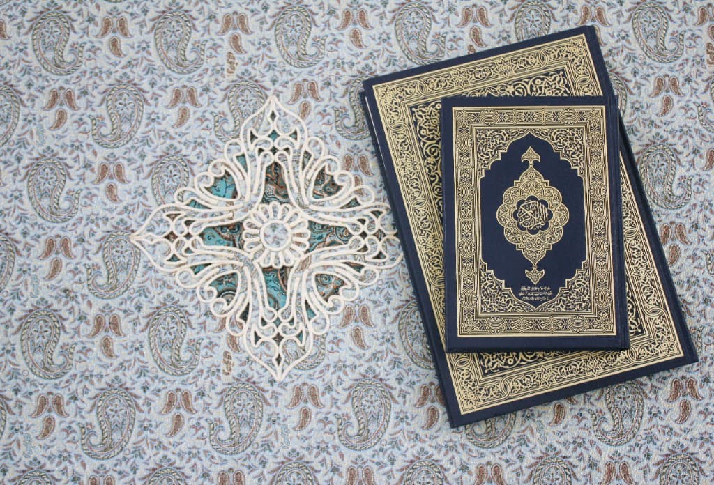 Ornate Qurans with gold calligraphy and decorative lattice on patterned fabric